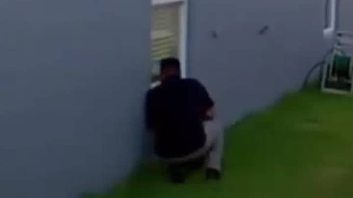 视频显示被定罪的杀手爬行在家庭的花园里看着窗户